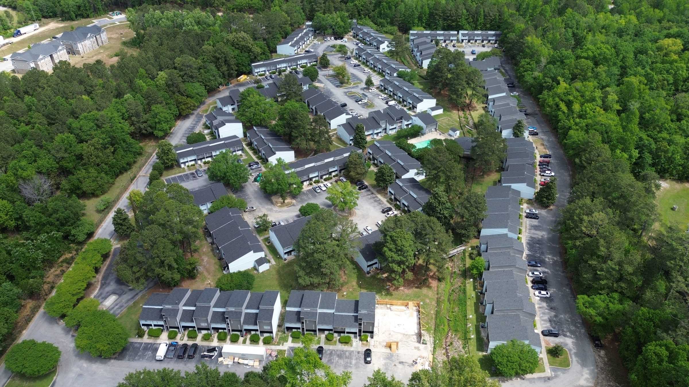 Drone view over an apartment community with rows of roofed buildings among trees.