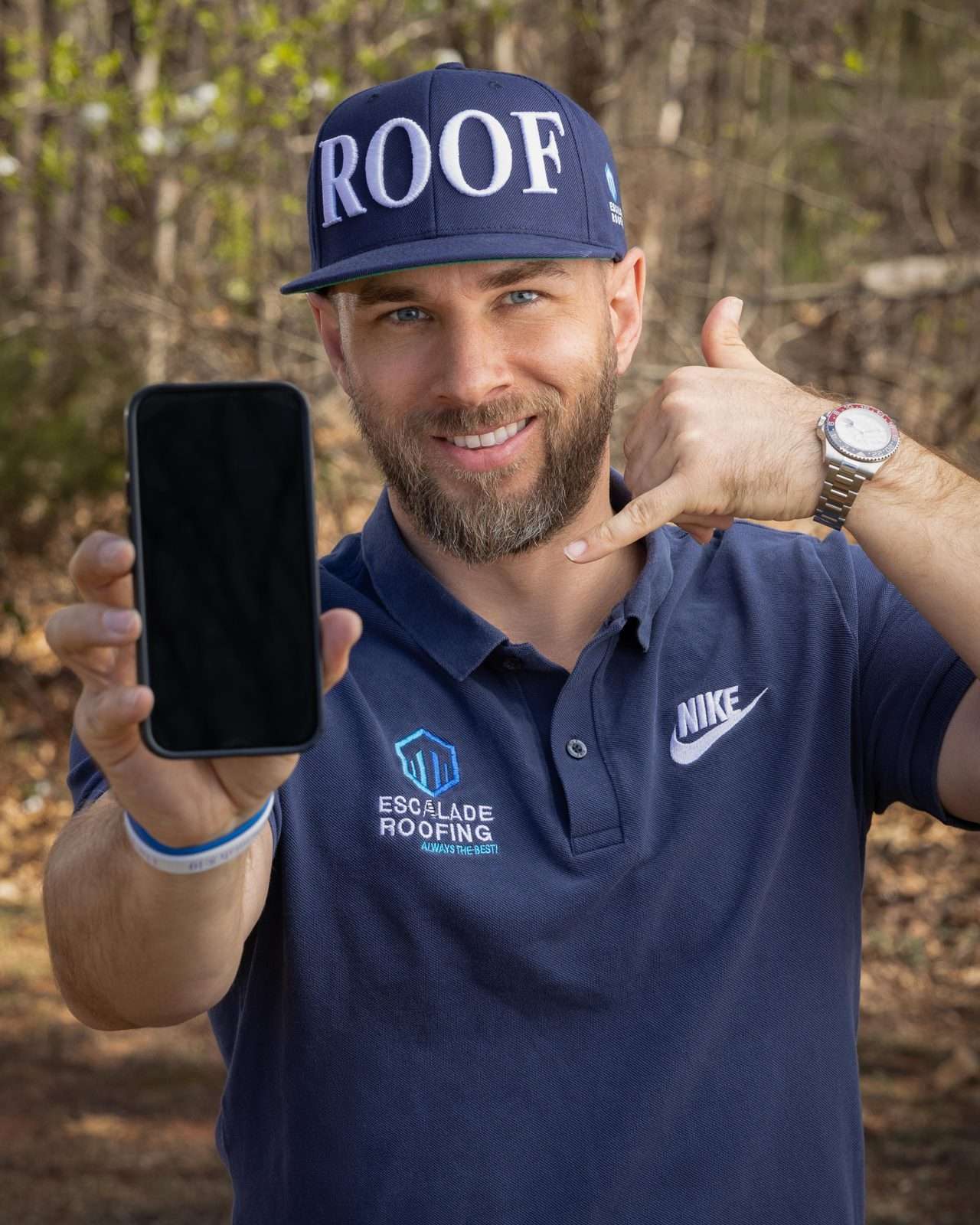 Cole Haynes, owner of Escalade Roofing, in an Escalade shirt and ROOF cap, holding up a phone and making a call-me sign.