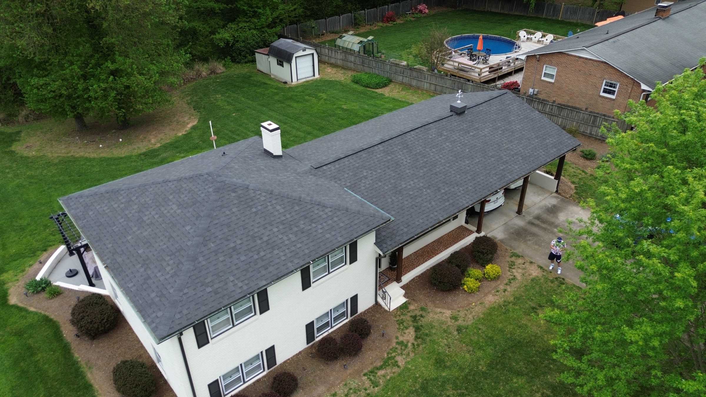 Drone view of a white split-level house with black shutters and a new gray shingle roof.