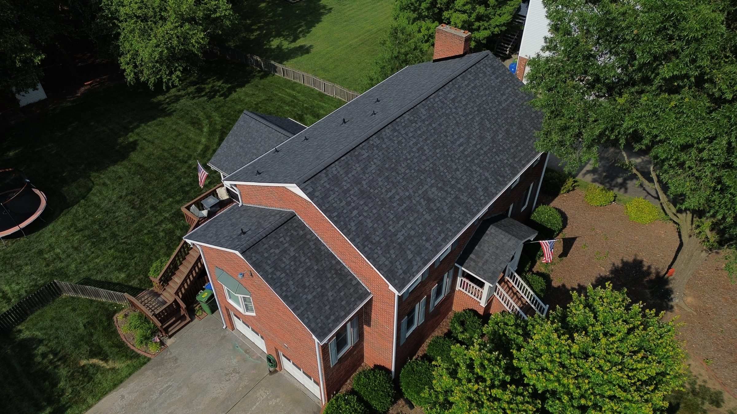 Drone view of a brick house on a slope with a new dark shingle roof.