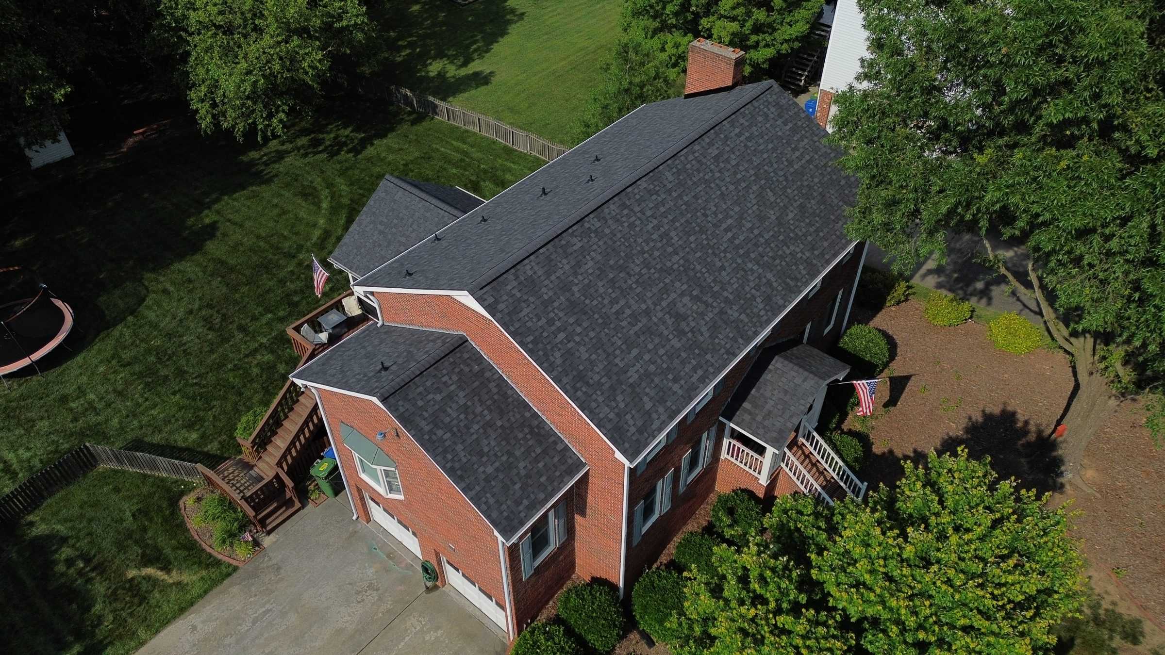 Drone view of a brick house on a slope with a new dark shingle roof.