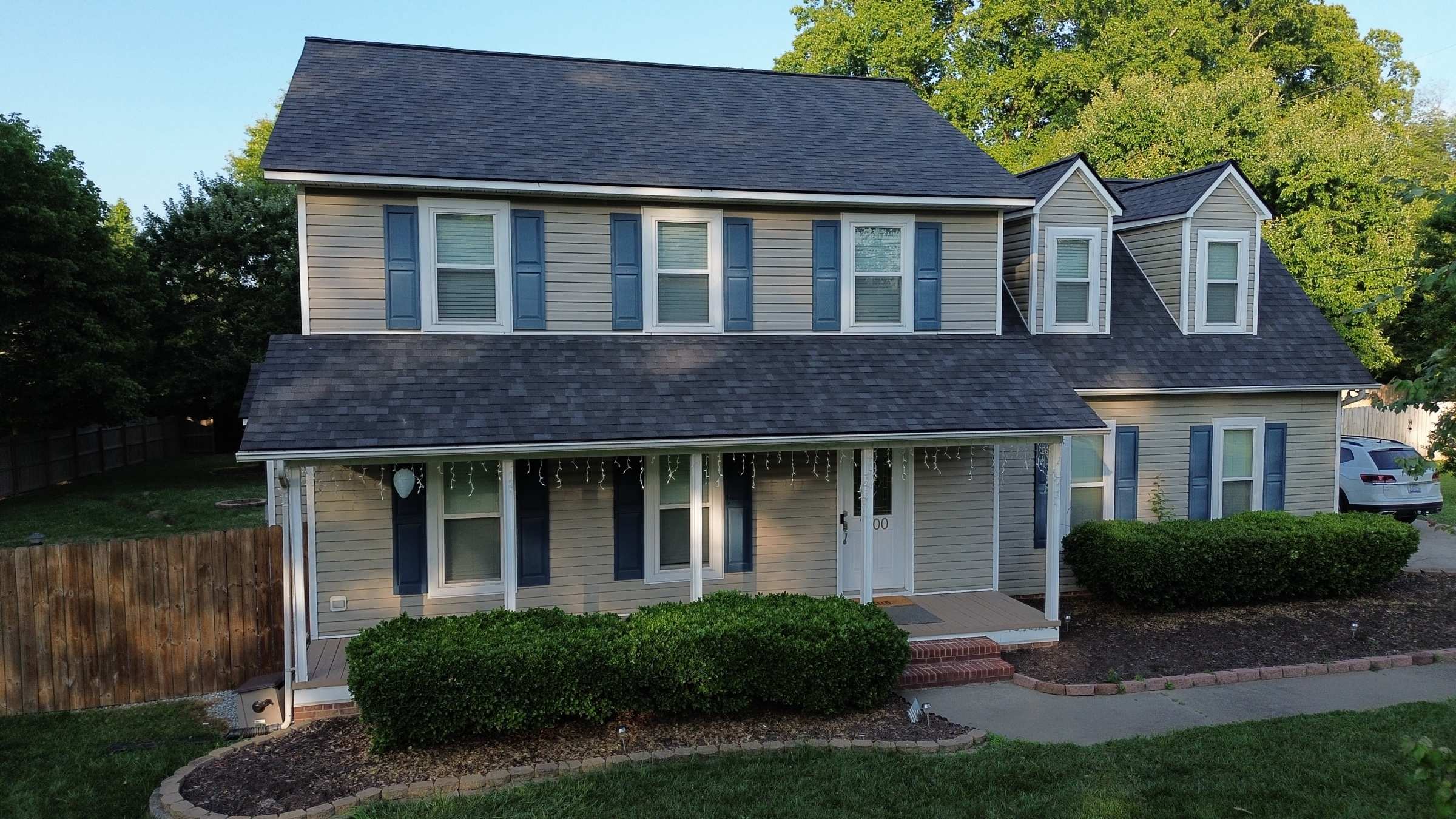 A two-story house with blue shutters, a front porch and a new dark shingle roof.