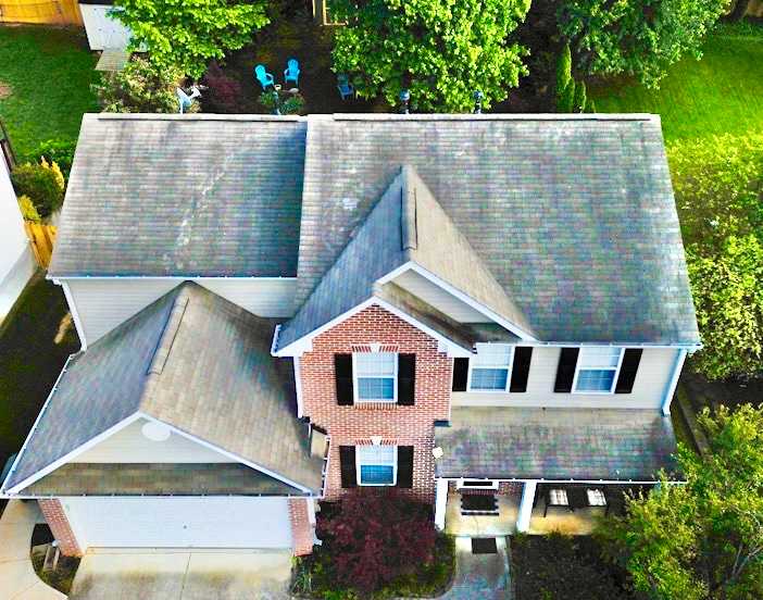 Drone view of a brick and siding two-story house with an old, weathered and stained shingle roof.